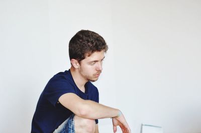 Thoughtful man looking away while sitting against white wall at home