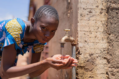 Girl drinking water from faucet against wall