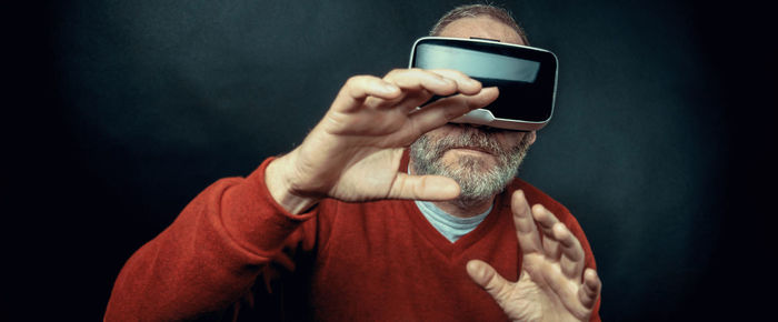 Panoramic view of senior man using virtual reality headset against black background