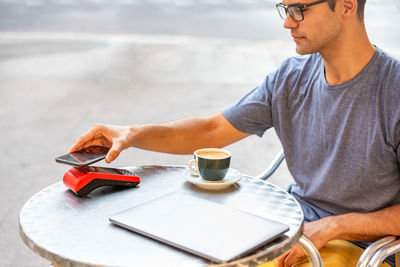 Youn latin man paying with mobile phone in the machine