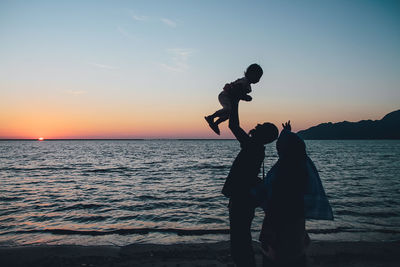 Parents with daughter at beach during sunset