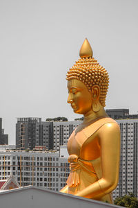 Buddha statue against buildings in city against sky