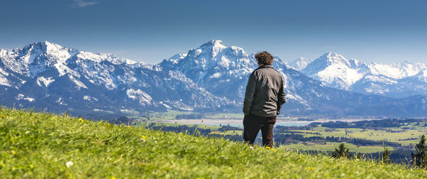Man standing on grassy field against snowcapped mountains