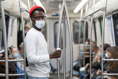 Black man wearing face mask as protection against covid virus, holding handrail in public transport