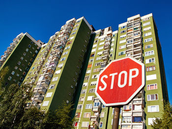 Low angle view of road sign by buildings against blue sky