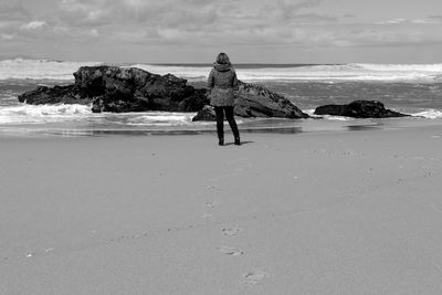 Rear view of woman standing at beach against sky