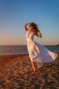 Beautiful slender woman in a white dress by the sea at sunset