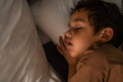 Little sleeping boy on the bed with a phone.