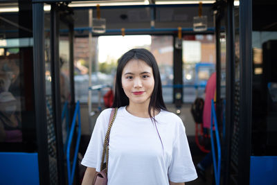 Portrait of smiling young woman standing against bus