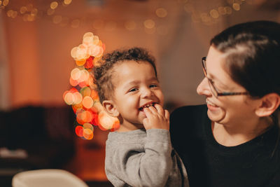 Close-up of mother with cute son against illuminated christmas lights at home