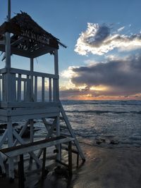 Built structure on beach against sky during sunset