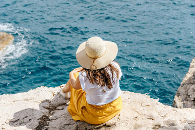 Rear view of woman sitting on rock by sea