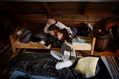 High angle view of friends watching movie over digital tablet while relaxing in cottage