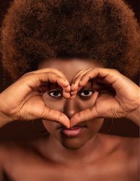 Close-up portrait of woman with curly hair making heart shape