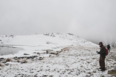 Hiker standing on snow covered mountain against sky