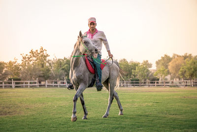 Full length of a young man riding horse on field