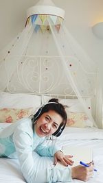 Portrait of smiling woman listening music while lying on bed at home