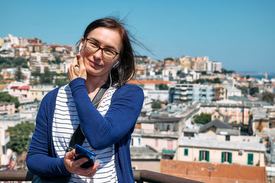 Happy smiling woman listening music, song or audio guide at mobile phone while enjoying a view