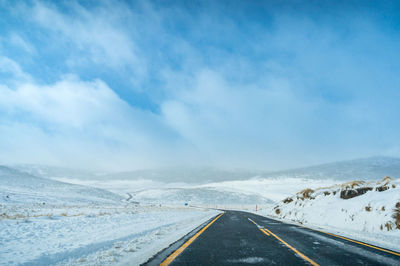 Road leading towards snowcapped mountain against sky