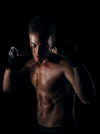 Portrait of shirtless man standing against black background