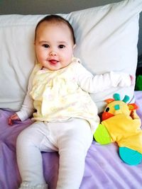 Portrait of cute baby girl sitting on bed at home