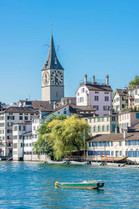 Sailboats in canal by buildings against clear blue sky