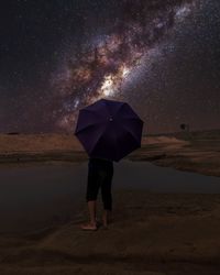 One men with an umbrella standing on the bank of a river on a under the sky full of star