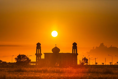 Silhouette people on field against orange sky