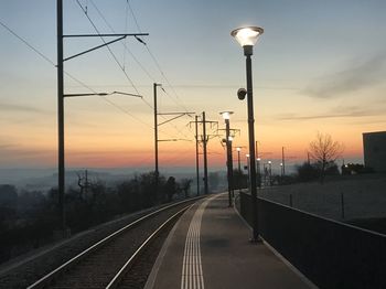 Illuminated gas lights by railroad tracks against sky during sunset