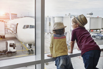 Two children wearing straw hats looking through window to airplane on the apron