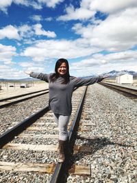 Portrait of smiling woman balancing on railroad track against sky