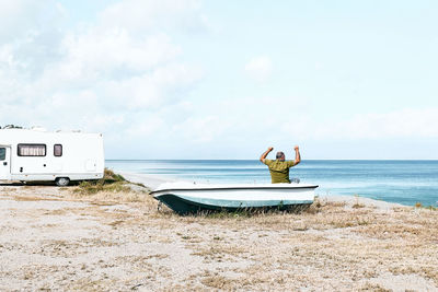 Man sitting in boat on the beach near his white camper van parked by the sea. sicily. ionian sea.