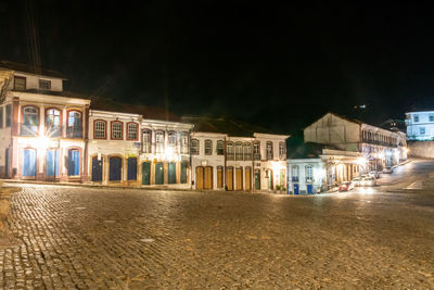 Illuminated buildings by street against sky at night