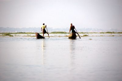 Fishermen in boat on sea against sky