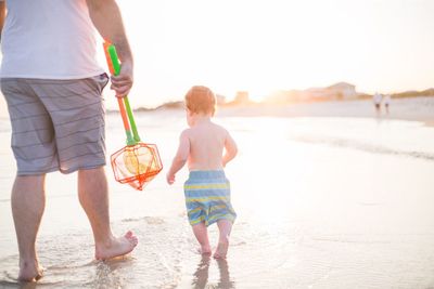 Low section of father with son on shore at beach