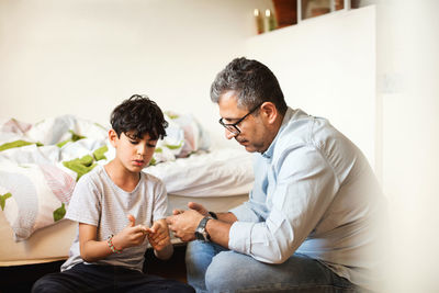 Father and son playing with rubber bands by bed at home