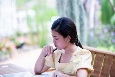 Young woman looking away while sitting on table