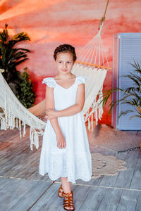 Girl in a white summer dress. boho style interior. beautiful summer area. indoor hammock. braids 