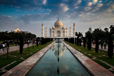 Reflection of taj mahal on reflecting pool against cloudy sky