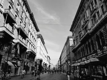 People on street amidst buildings in city against sky