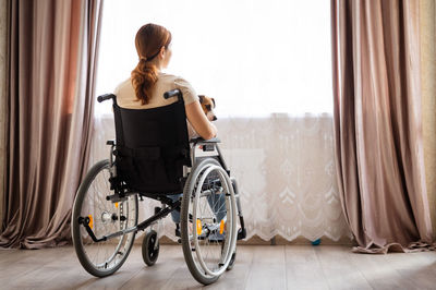 Side view of young woman sitting on wheelchair at home