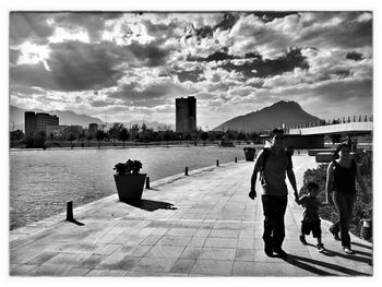People walking in city against cloudy sky
