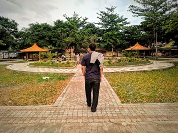 Rear view of man walking on footpath against sky