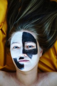 Portrait of shirtless woman with painted face lying on bed