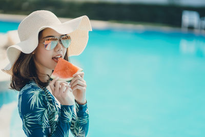 Portrait of young woman eating watermelon sitting by swimming pool