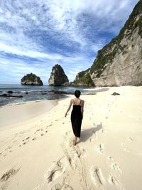 Rear view of woman standing at beach against sky