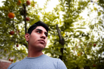 Portrait of young man looking away against trees