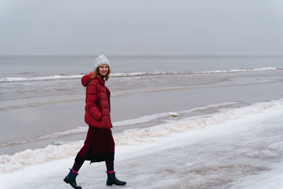 A woman in red warm clothes walks along the sea in winter