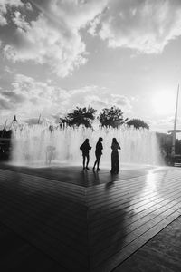 Rear view of people by swimming pool against sky