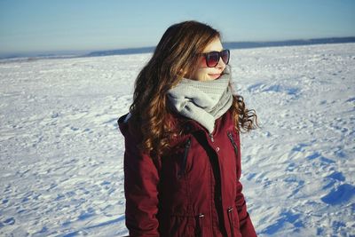 Beautiful young woman wearing muffler and jacket on snowy field against sky